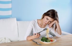 Young depressed girl with eating disorder at wooden table.